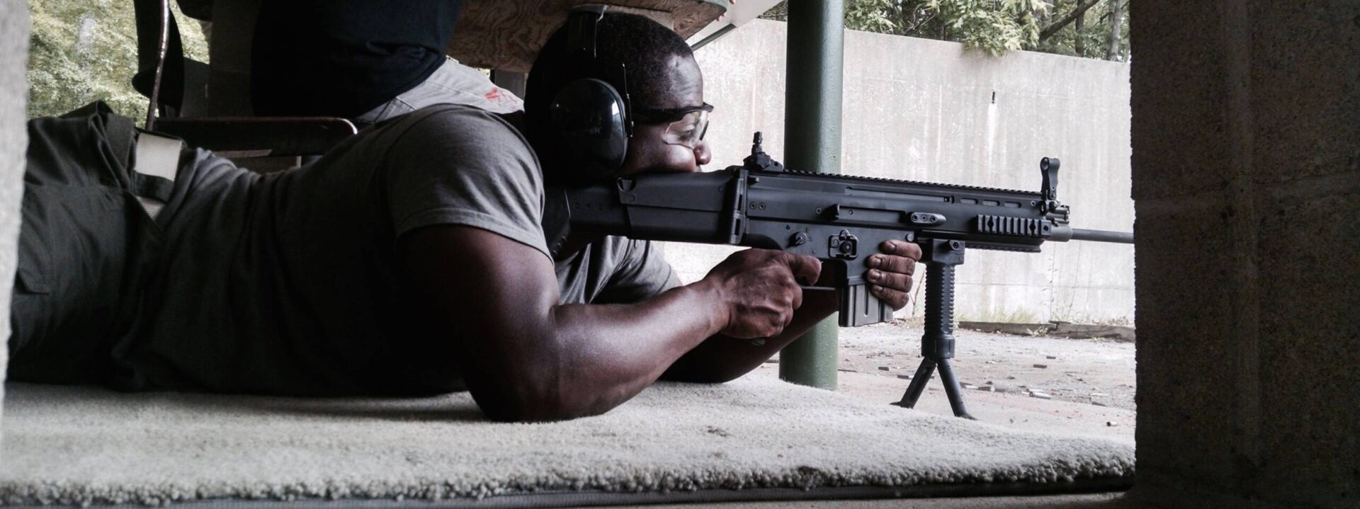 A man is holding an ar-1 5 rifle and wearing ear muffs.