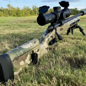 A rifle with a scope and bipod in the grass.